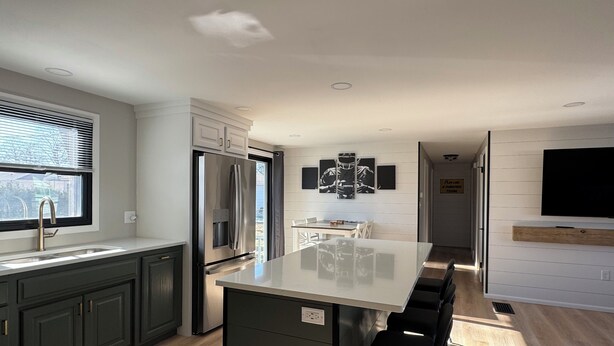 Una cocina moderna con una isla central, electrodomésticos de acero inoxidable y un comedor con televisor montado en la pared.