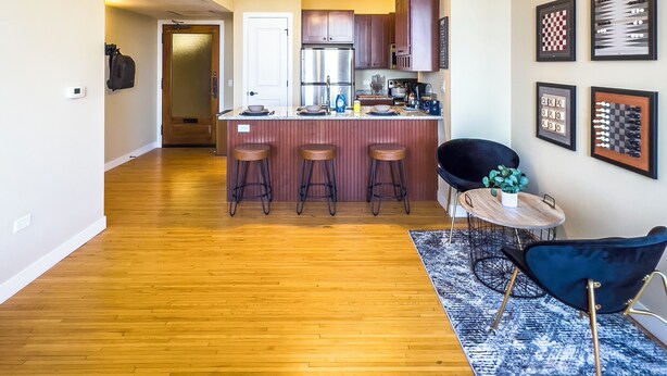 A spacious living area with a kitchen in the background, wooden flooring, and a blue patterned rug. - River Views and FREE Parking! (Saint Paul)