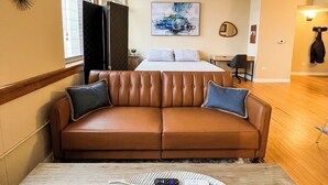 A modern hotel room with a brown leather sofa, a wooden coffee table, and a large bed with a blue and white abstract painting above it. - River Views and FREE Parking! (Saint Paul)