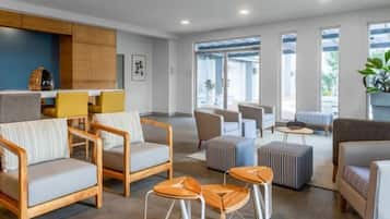 Un moderno vestíbulo de hotel con espacios de estar, una zona de cocina y grandes ventanales.