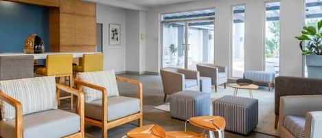 A modern hotel lobby with seating arrangements, a kitchen area, and large windows.