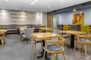 A modern dining area with wooden tables and chairs, a grey cushioned bench, and pendant lighting. - Holiday Inn Express SAN JOSE FORUM by IHG (Pozos)