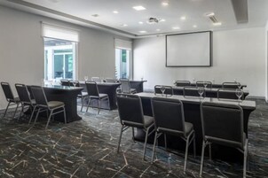 Un salón de conferencias con una mesa larga, varias sillas y una pantalla para proyector.