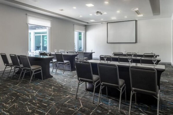 Una sala conferenze con un lungo tavolo, diverse sedie e uno schermo per proiettore.
