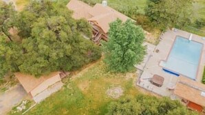 A residential property with a swimming pool, a fenced yard, and a large tree.