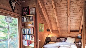 A cozy log cabin bedroom with a large bookshelf, a bed with a furry rug, and a window overlooking greenery. - Zirbenwaldhütt´n by Interhome (Turracher Höhe)