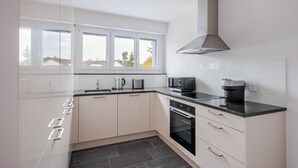 A modern kitchen with white cabinets, a black countertop, a built-in oven, a microwave, a kettle, and a coffee maker. - Blueground | Dietikon, balcony, nr Lindenplatz (Zurich)