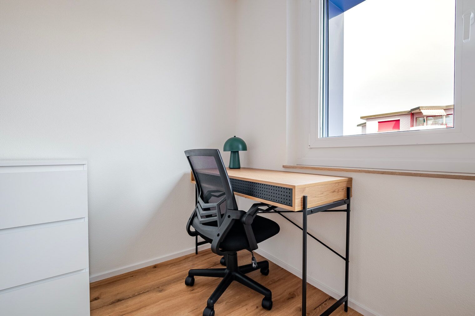 Ein Zimmer mit Ecke, Schreibtisch, Stuhl und Fenster.