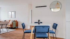 Una sala de estar moderna con una mesa redonda blanca, sillas de terciopelo azul, un sofá con cojines, una mesita de centro y un espejo en la pared.
