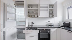 Una cocina moderna con armarios blancos, horno empotrado, microondas y cafetera.