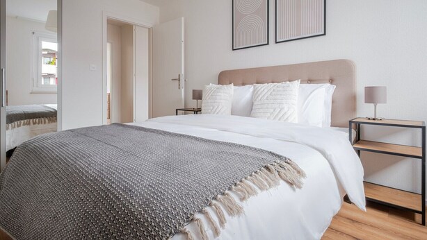 Un dormitorio moderno con una cama grande, una mesita de noche con lámpara y dos cuadros enmarcados en la pared.