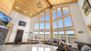A spacious living area with large windows, a wooden ceiling, and a view of the outdoors. - Eagle Eye Retreat: AC, EV, Hot tub, Minutes to reservoir, 35 miles to W Yellowstone (Island Park)
