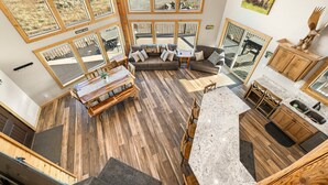 A spacious living area with large windows, a wooden floor, a dining table, and a kitchen area. - Eagle Eye Retreat: AC, EV, Hot tub, Minutes to reservoir, 35 miles to W Yellowstone (Island Park)