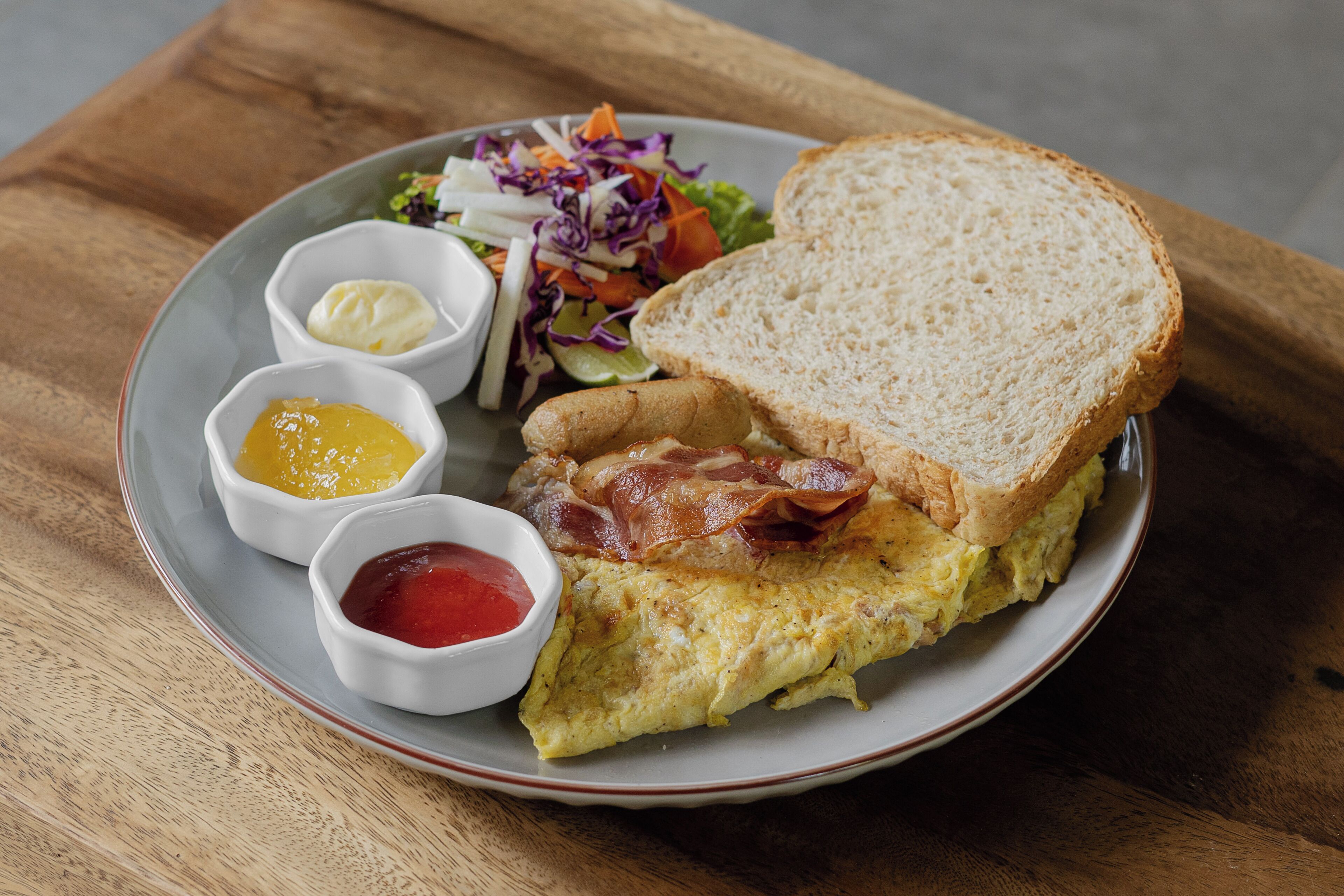 A plate with an omelette, bacon, toast, and a side salad with coleslaw.