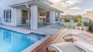 Une maison moderne dotée d’une piscine, d’un patio avec des chaises et d’un espace extérieur couvert.