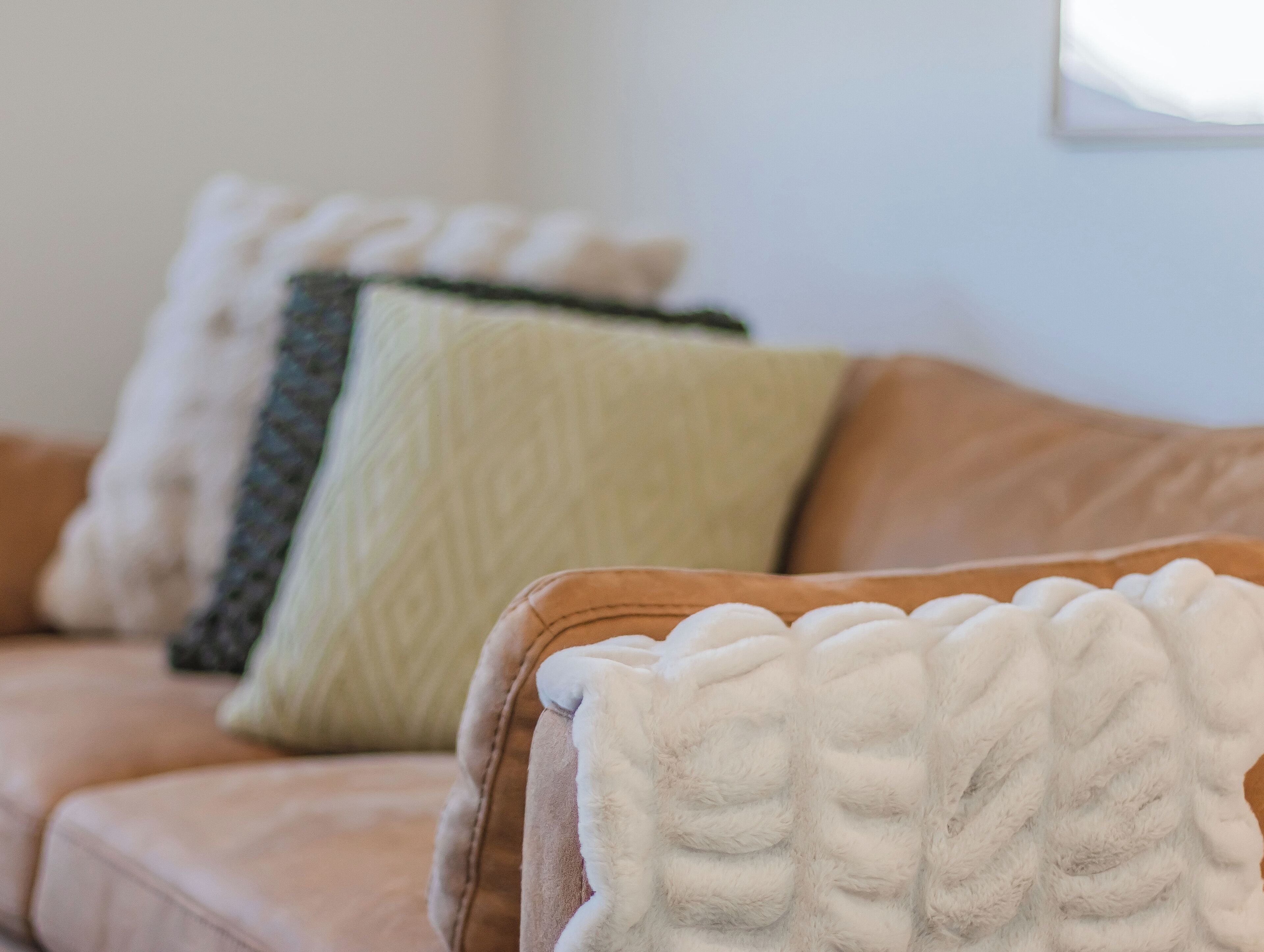 A beige sofa with a white textured throw blanket and a green quilted pillow.
