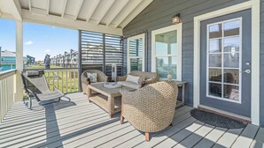 Eine überdachte Terrasse mit Korbmöbeln, einem Esstisch und Blick auf die Nachbarschaft.