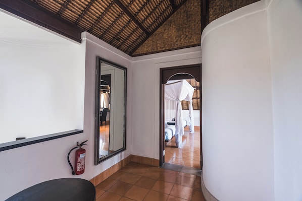 A hallway with a fire extinguisher, a mirror, and a bed with a canopy in the background.