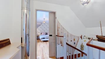 Corredor que dá para um quarto com cama, escada de madeira e grade decorativa de rede.