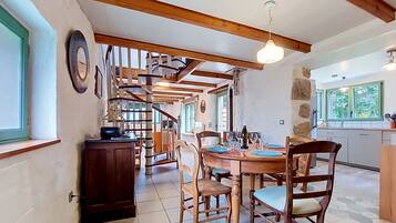 Uma sala de jantar com escada de madeira, cozinha com paredes de pedra e vista para o verde lá fora.