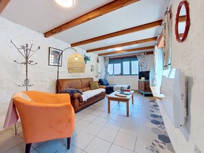 A living room with a brown leather sofa, an orange armchair, a wooden coffee table, a TV, and a fireplace.