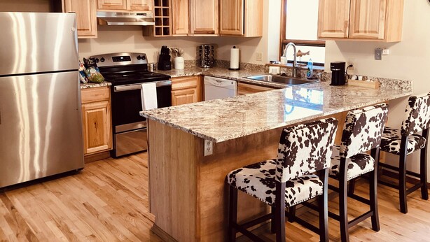 A modern kitchen with wooden cabinets, stainless steel appliances, a granite countertop, and a cow print bar stool. - Serene 4-bedroom house in Durango (Durango)