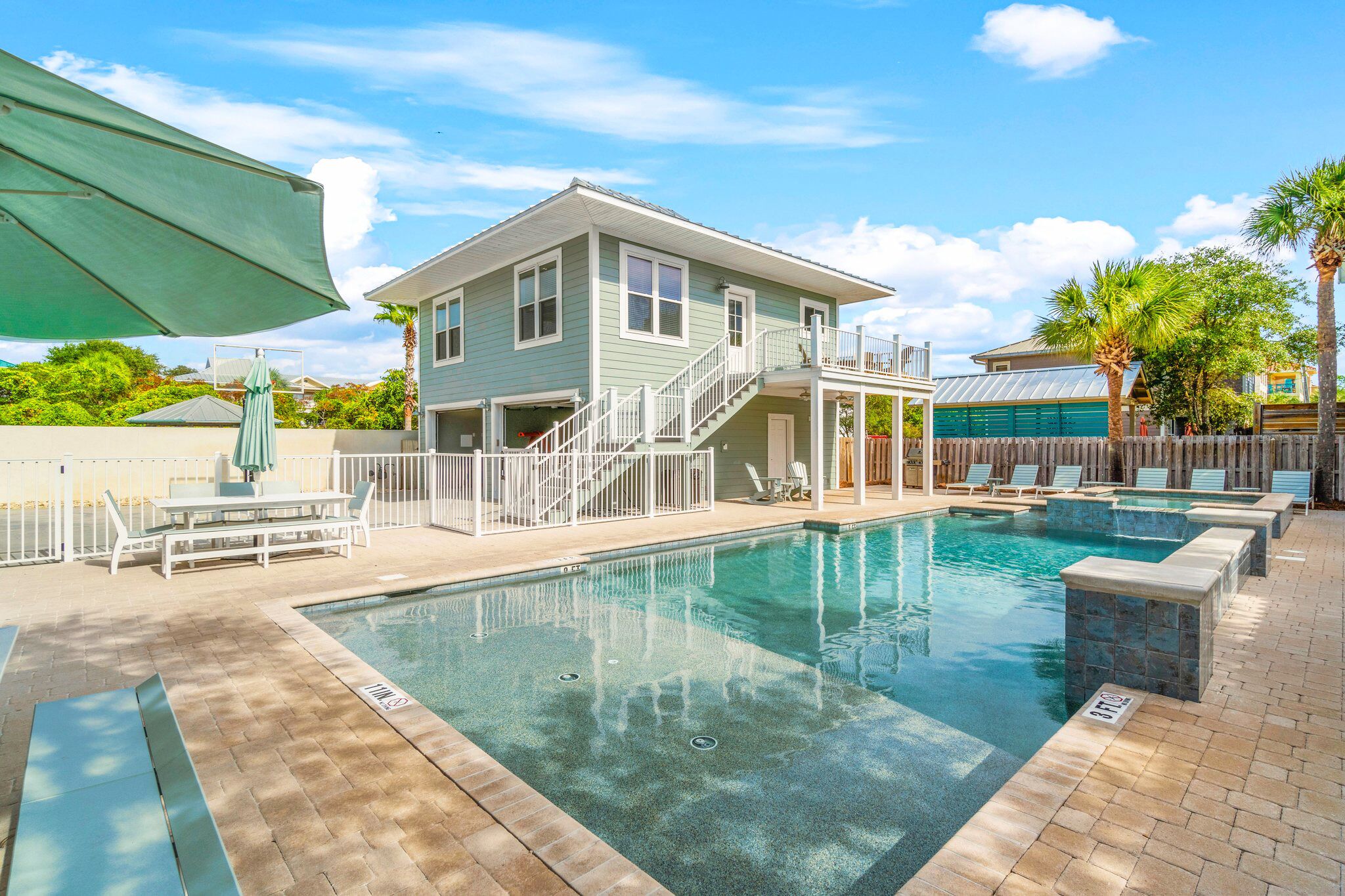 A pool area with a two-story building, a covered seating area, and a fenced deck.