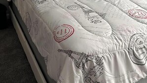 A bed with a white duvet featuring a cityscape and Eiffel Tower design, a grey headboard, and matching pillows. - Charming apartment in a great location. Near to the fun of Hartford (Hartford)