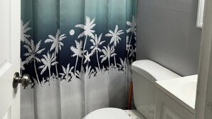 A bathroom with a toilet, a shower curtain with a palm tree design, and a white sink. - Charming apartment in a great location. Near to the fun of Hartford (Hartford)