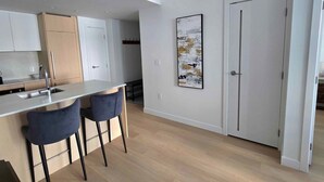 Une cuisine moderne avec un îlot central, deux tabourets de bar et un tableau accroché au mur.