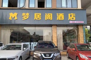 Un hotel con un cartel grande que muestra su nombre y número de contacto. Hay varios coches estacionados al frente.