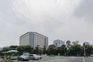 Un edificio de varios pisos con estilo arquitectónico moderno, situado en una transitada intersección con vehículos y un paso de peatones.