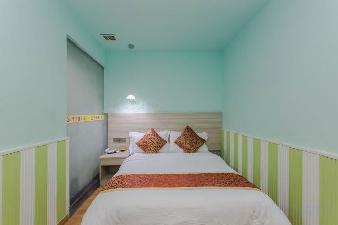 A narrow hotel room with a single bed, a nightstand, and a wall-mounted telephone.