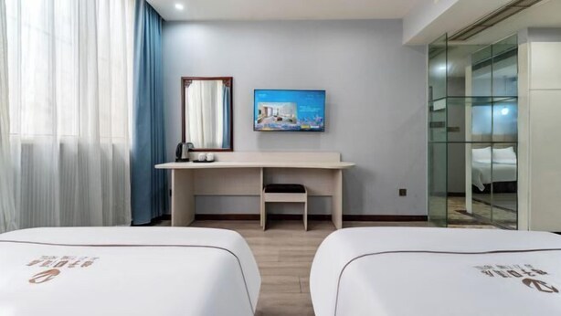 Habitación de hotel con dos camas, un escritorio, una silla, un televisor y un ventanal con cortinas.