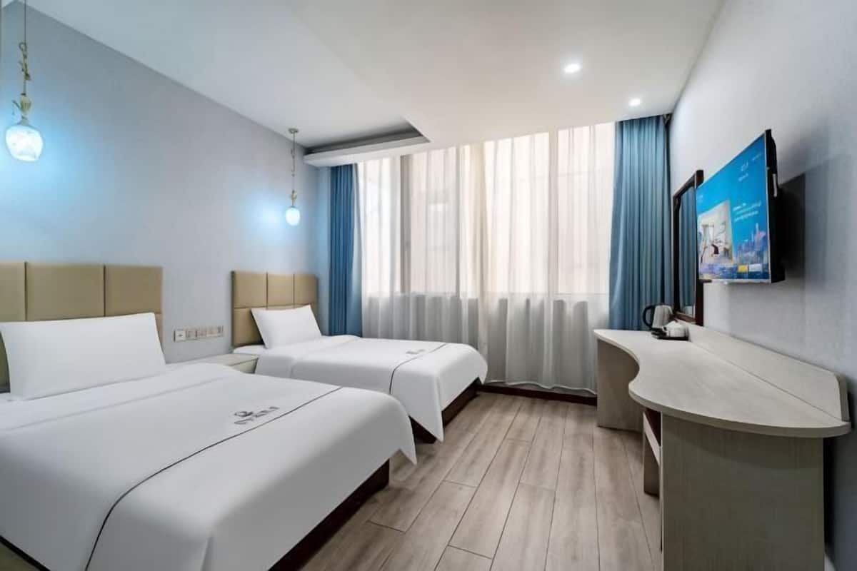 Une chambre d’hôtel avec deux lits, un bureau, une télévision et une grande fenêtre avec des rideaux.