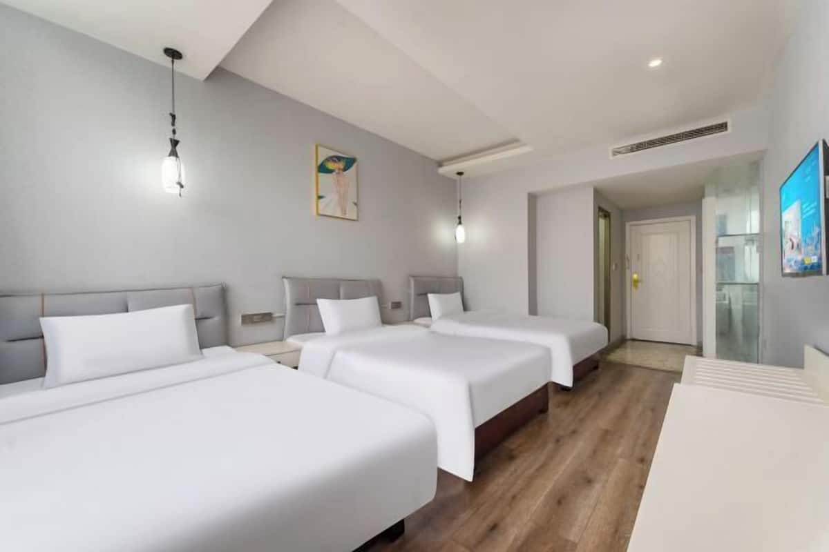 Une chambre d’hôtel avec trois lits, un plancher en bois, un tableau accroché au mur et une porte donnant sur une autre pièce.