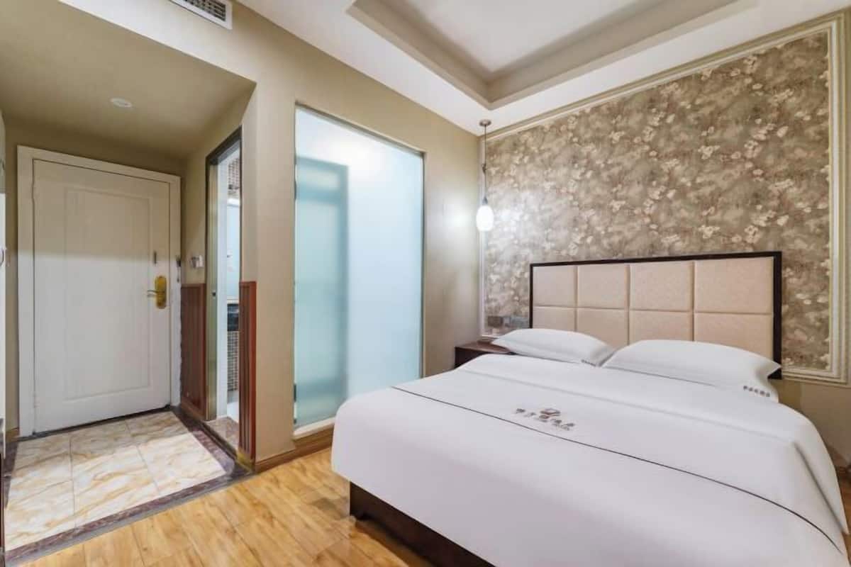 Une chambre d’hôtel comprenant un lit, une table de chevet, une lampe fixée au mur et une porte donnant sur une autre pièce.