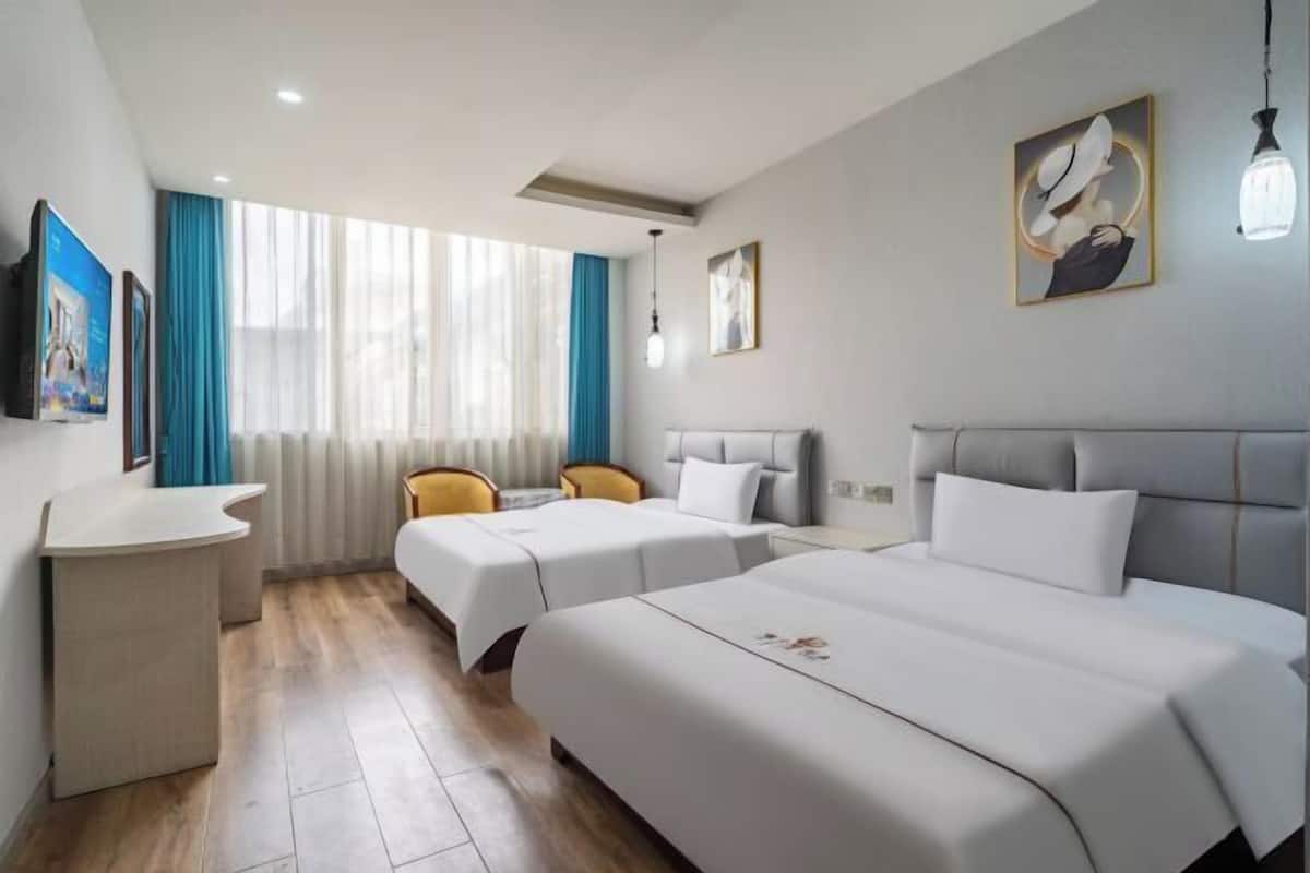 Une chambre d’hôtel avec deux lits, un bureau et une fenêtre avec des rideaux.