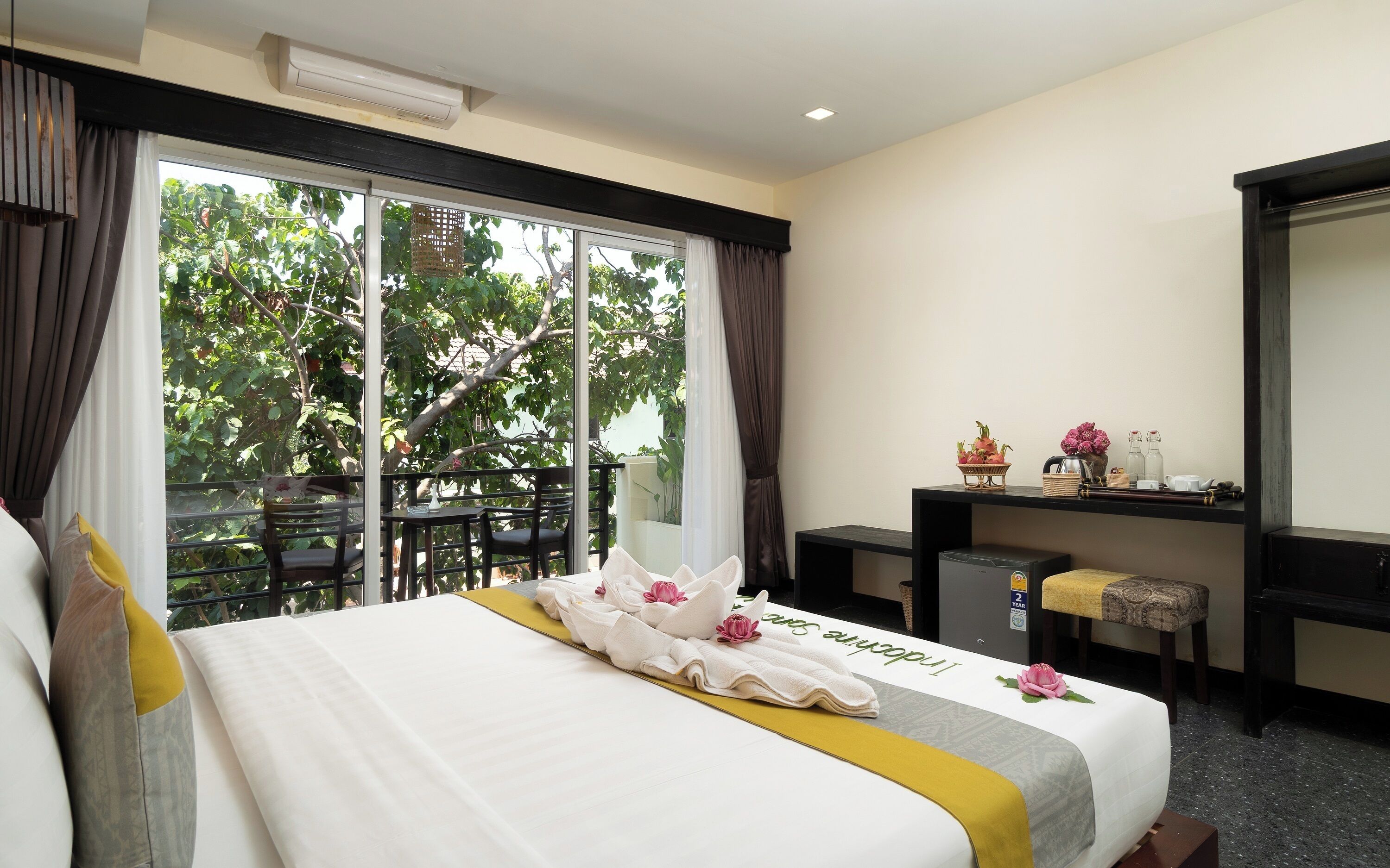 A hotel room with a large bed, a desk with a chair, a small table, and a mirror.