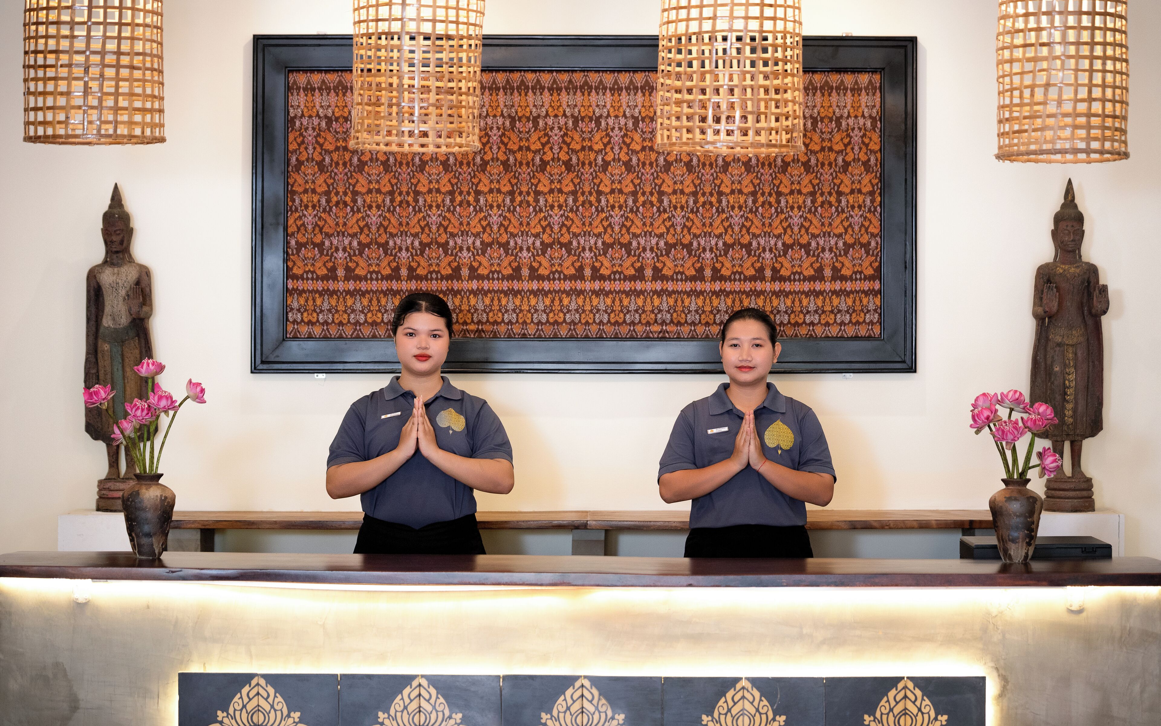 Two receptionists at a reception desk with a large patterned tapestry and two statues on either side.