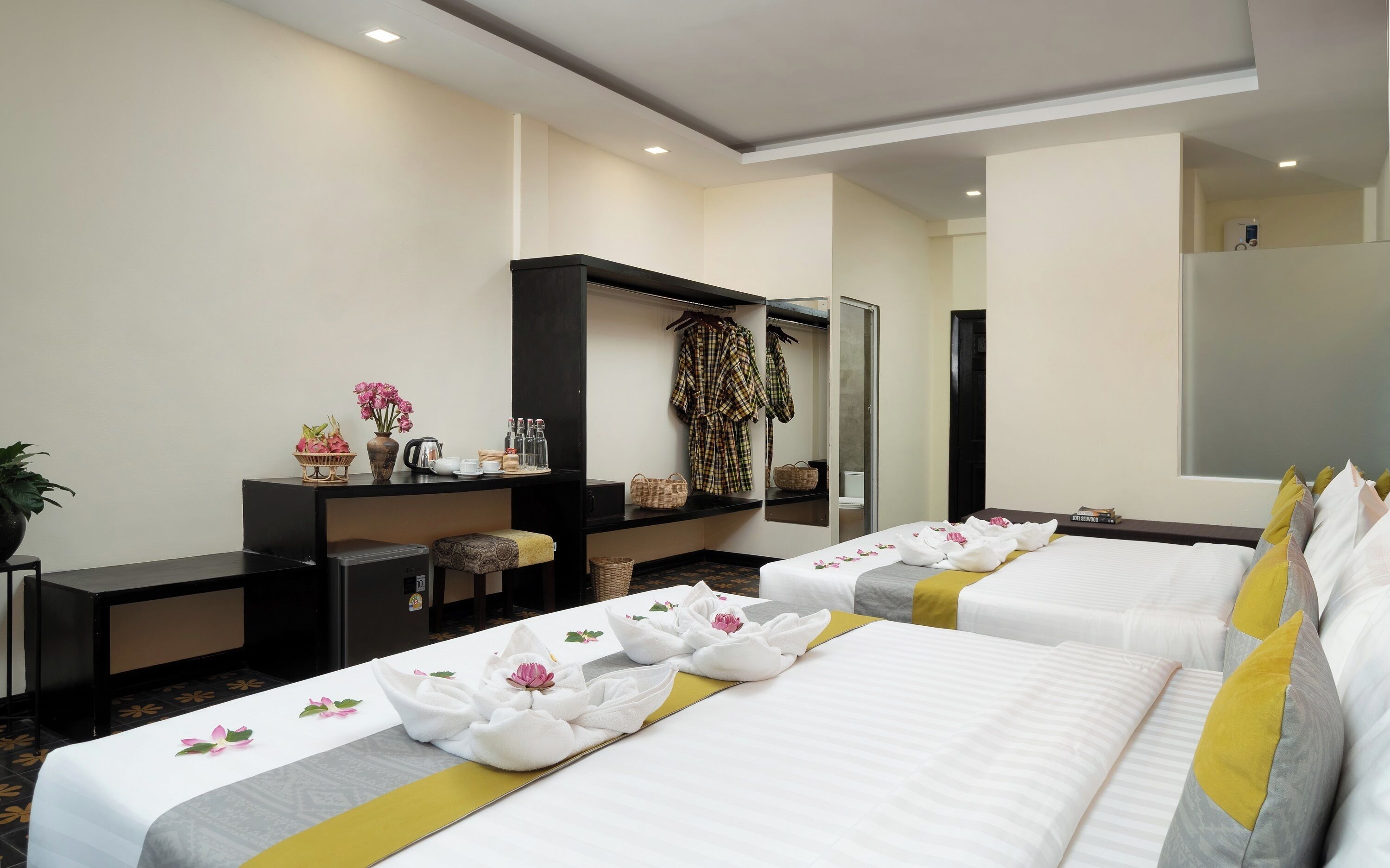 A hotel room with two beds, a desk with a computer, a wardrobe, and a mirror.