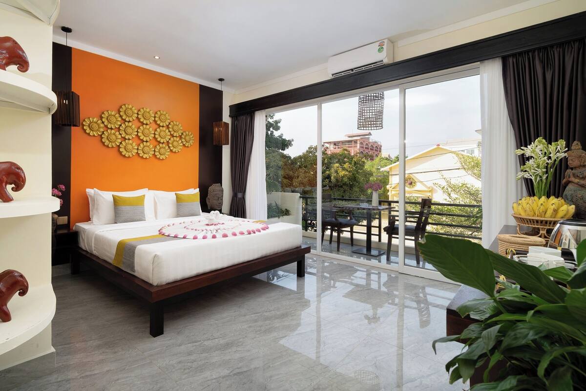 Une chambre d’hôtel moderne dotée d’un grand lit, d’un balcon avec un coin repas et d’œuvres d’art décoratives sur les murs.