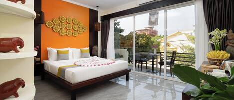 A modern hotel room with a large bed, a balcony with a dining area, and decorative wall art.