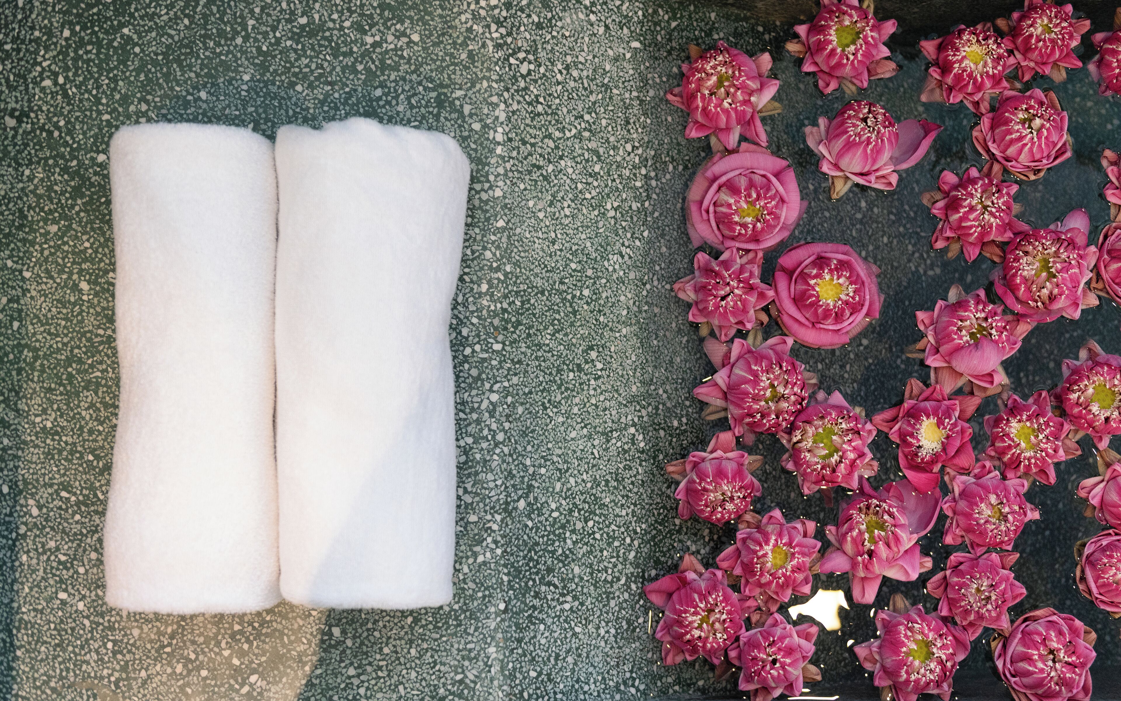 A pair of white towels and pink flowers on a terrazzo floor.