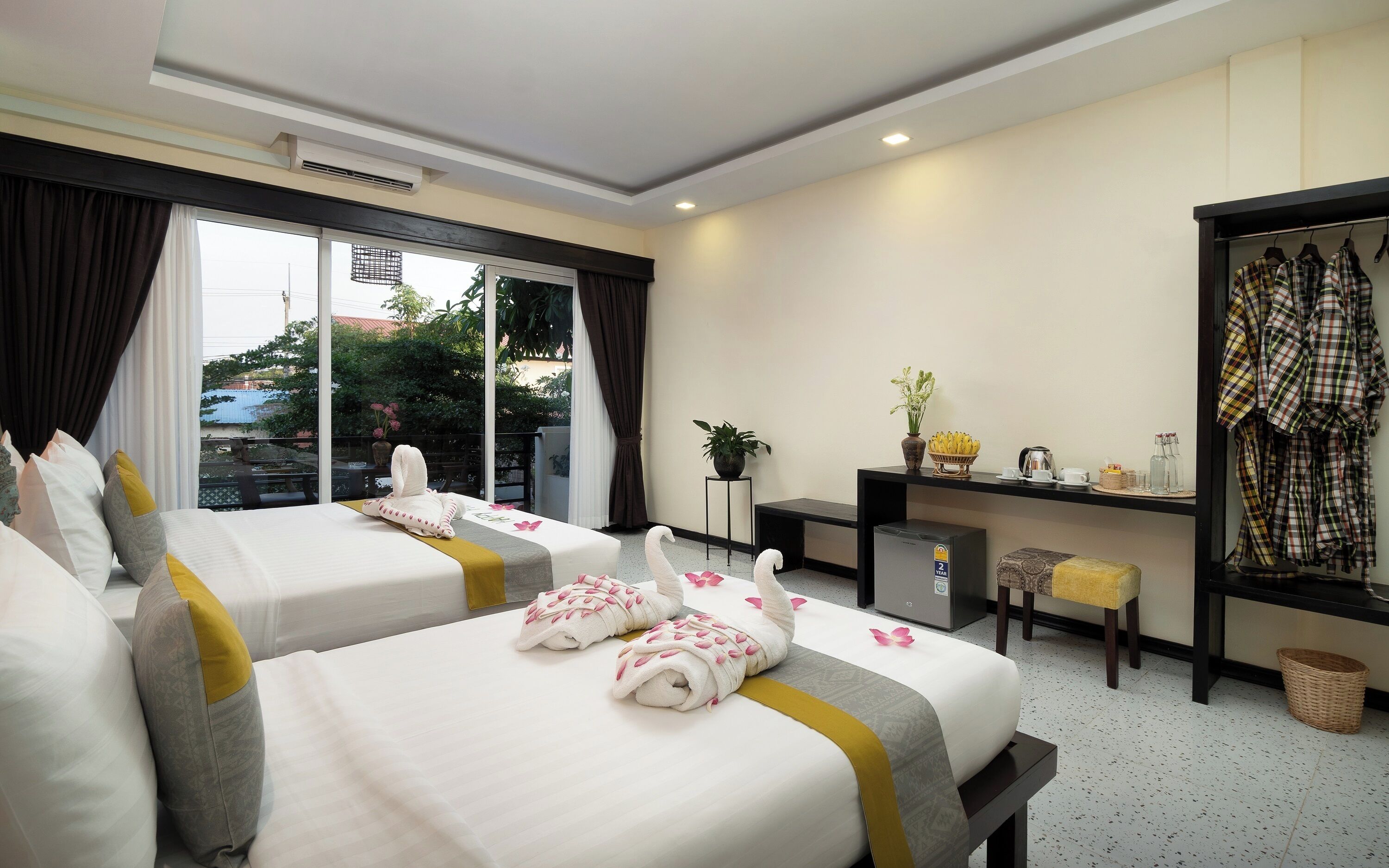 A hotel room with two beds, a desk, a chair, a wardrobe, and a balcony with curtains.