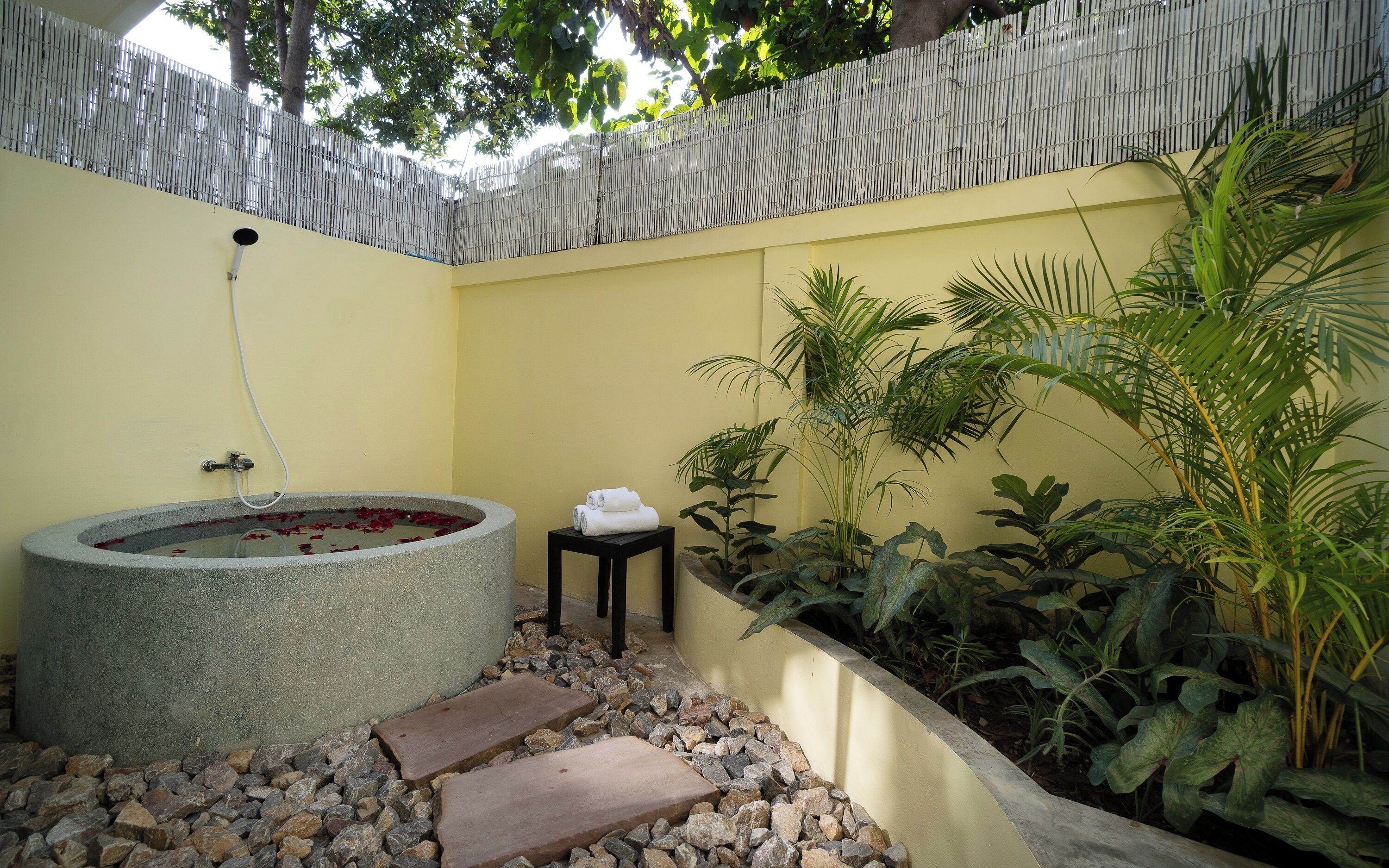 A spa area with a stone hot tub, a small table with towels, and a variety of plants.