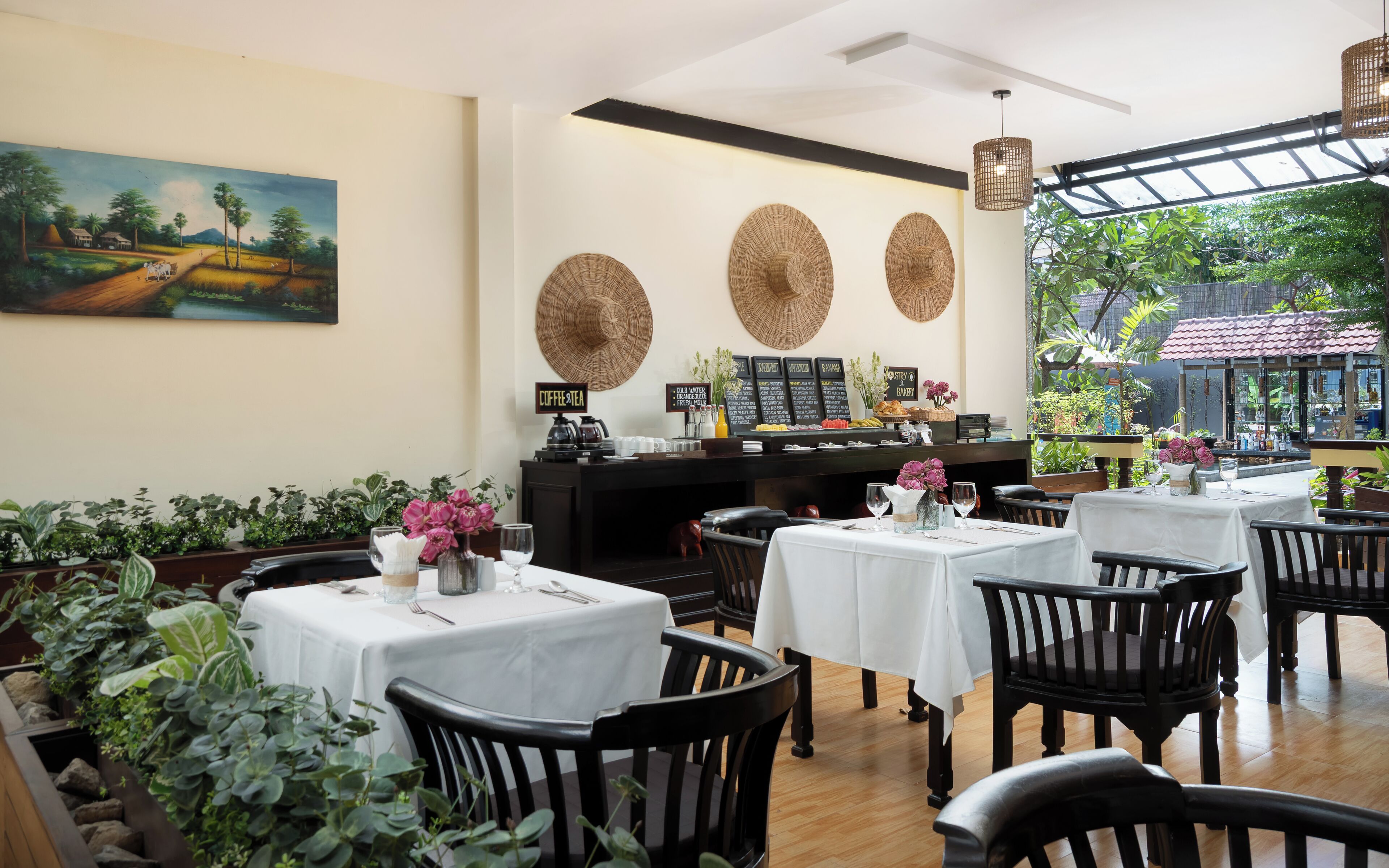 A restaurant with tables set for dining, a coffee station, and a view of greenery outside.