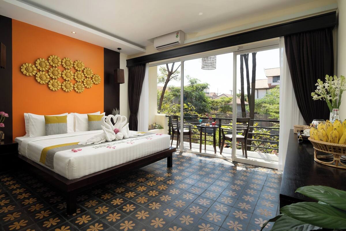 Une chambre d’hôtel comprenant un lit, un mur décoratif, un balcon avec une table et des chaises, et une vue sur l’extérieur.