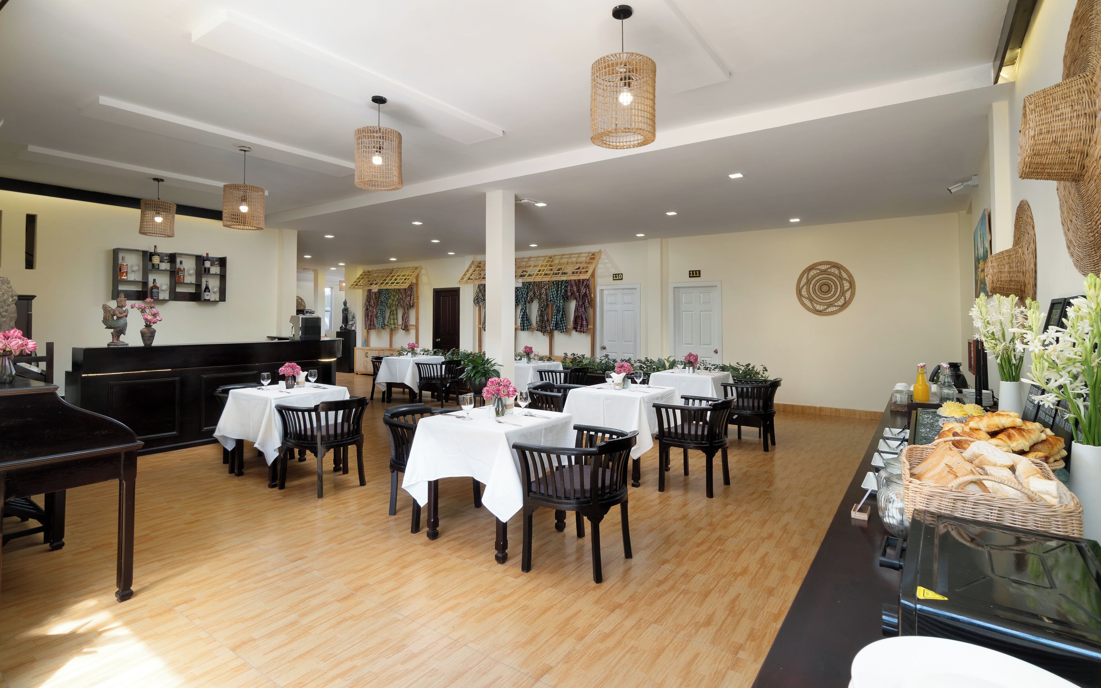 A dining area with multiple tables and chairs, a piano, and a buffet with bread and flowers.