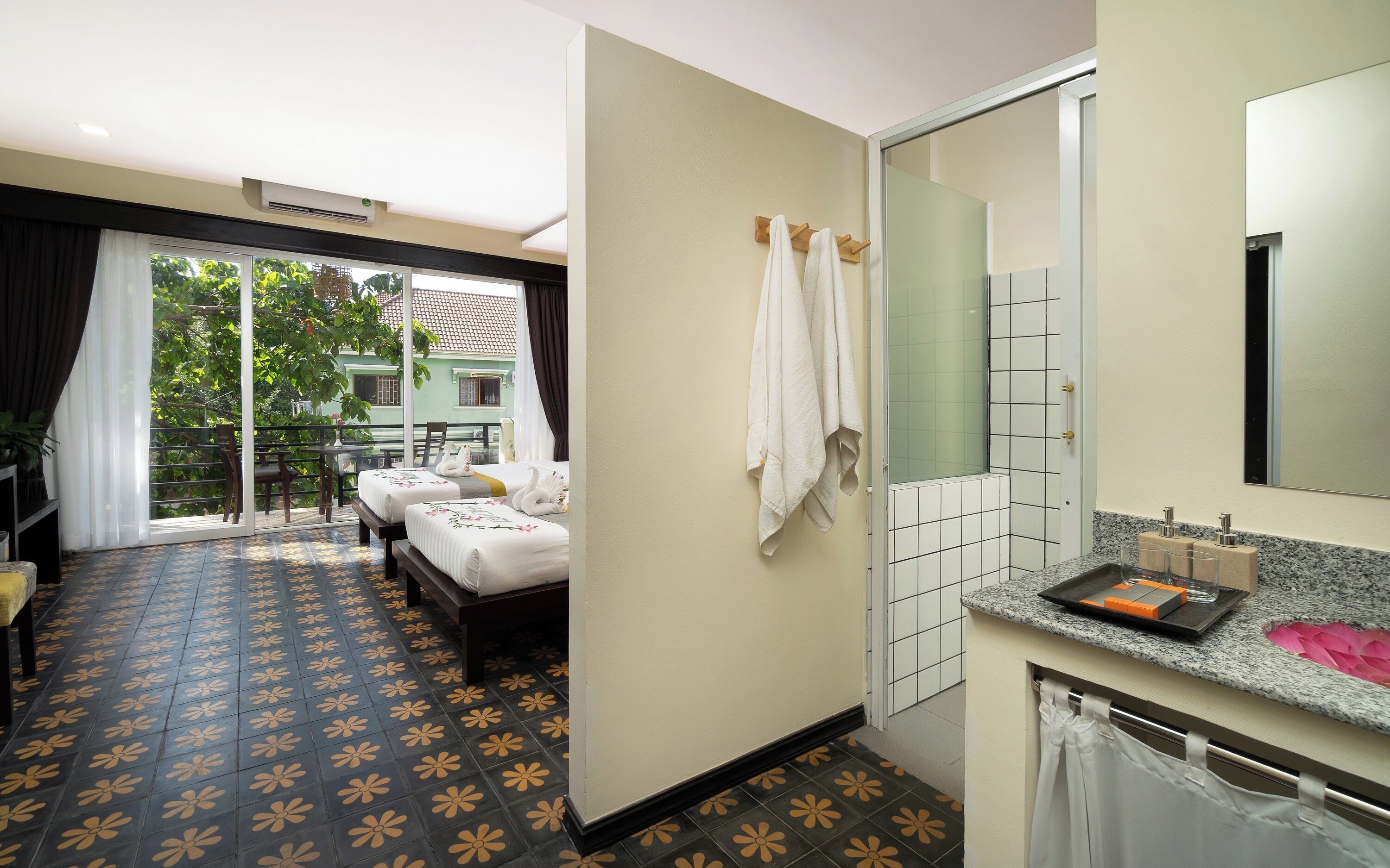 Habitación de hotel con balcón, dos camas, baño con espejo y lavamanos.